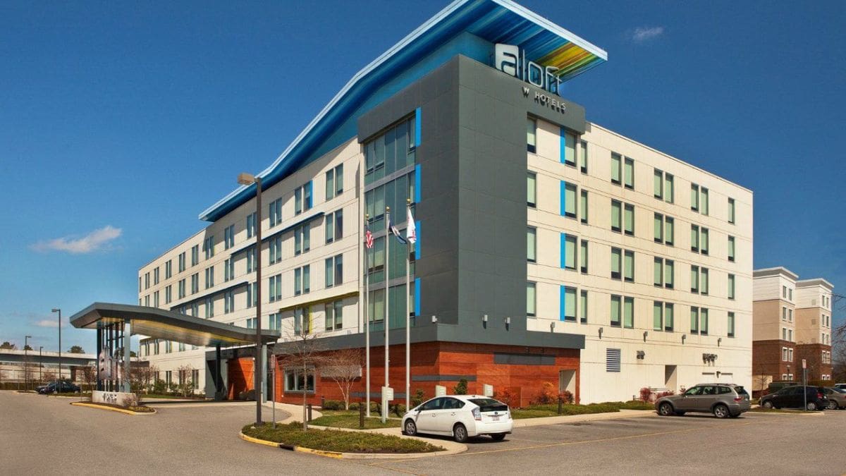 Modern multi-story hotel building with flags and parked cars.