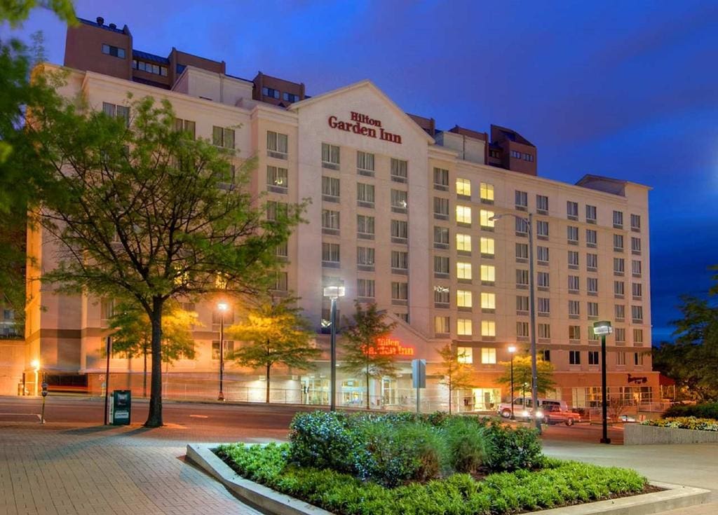 Hilton Garden Inn hotel illuminated at dusk with surrounding greenery.